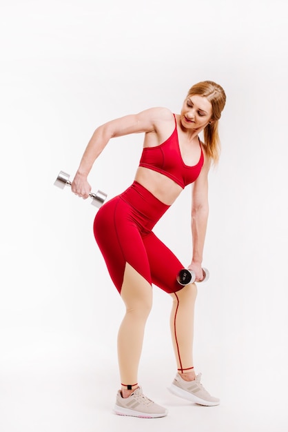 Young strong and sporty woman in red cloth doing exercises with dumbbells on white background