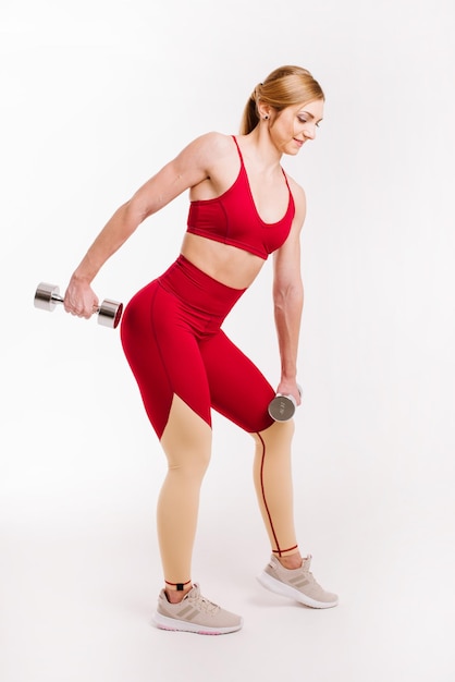 Young strong and sporty woman in red cloth doing exercises with dumbbells on white background