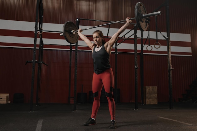 Young strong woman holding heavy barbell overhead Sports woman doing exercise