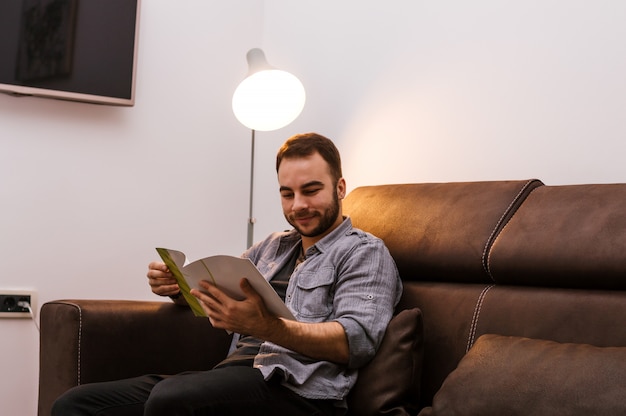 Young stubble man indoor reading magazine