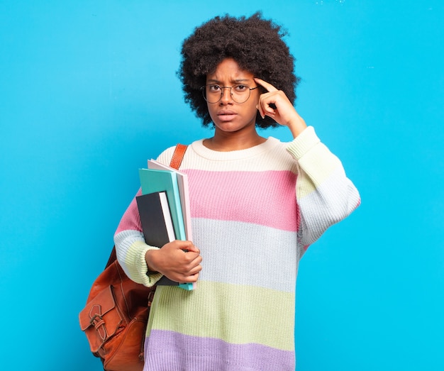 Giovane studentessa afro che si sente confusa e perplessa, mostrando che sei pazzo, pazzo o fuori di testa