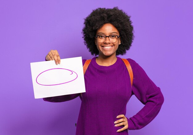 Young student afro woman smiling happily with a hand on hip and confident, positive, proud and friendly attitude