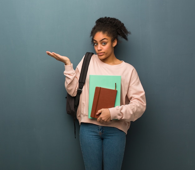 Young student black woman confused and doubtful. She is holding books.