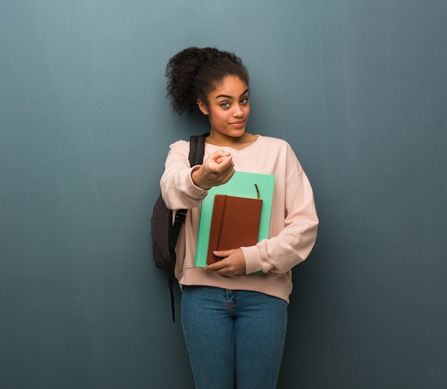 Young student black woman inviting to come. She is holding books.