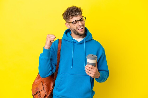 Uomo biondo giovane studente isolato su sfondo giallo che celebra una vittoria