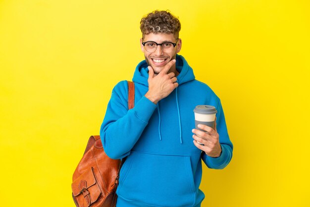 幸せで笑顔の黄色の背景に分離された若い学生のブロンドの男