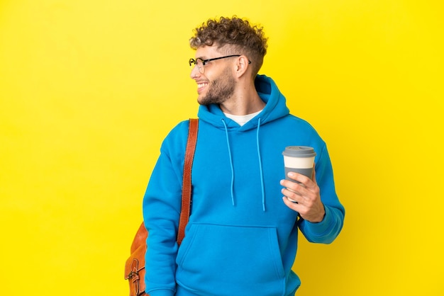 Young student blonde man isolated on yellow background laughing in lateral position