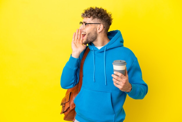 Young student blonde man isolated on yellow background shouting with mouth wide open to the side