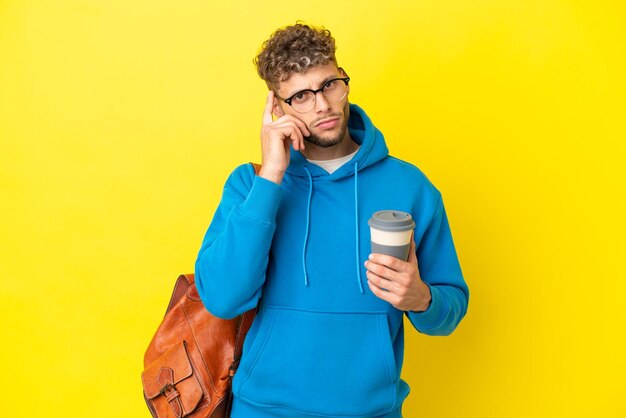 アイデアを考えて黄色の背景に分離された若い学生のブロンドの男