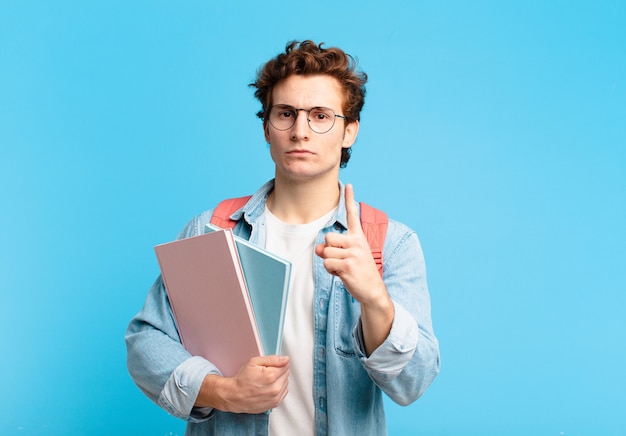 Young student boy feeling angry, annoyed, rebellious and aggressive, flipping the middle finger, fighting back