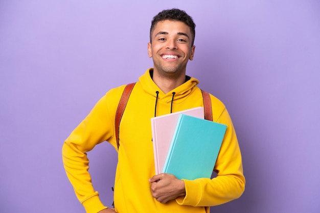 Foto giovane studente brasiliano uomo isolato su sfondo viola in posa con le braccia all'anca e sorridente