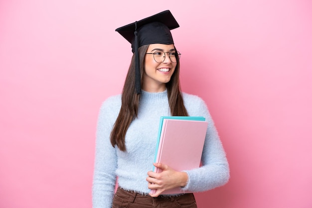 젊은 학생 브라질 여자 졸업 모자를 쓰고 분홍색 배경 찾고 측면에 고립