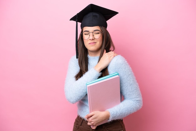 Молодая студентка из Бразилии в шляпе с дипломом, изолированная на розовом фоне, страдает от боли в плече за то, что приложила усилия