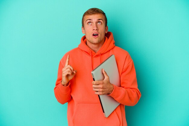 Young student caucasian man holding a laptop isolated on blue background