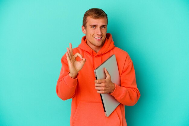 Young student caucasian man holding a laptop isolated on blue background