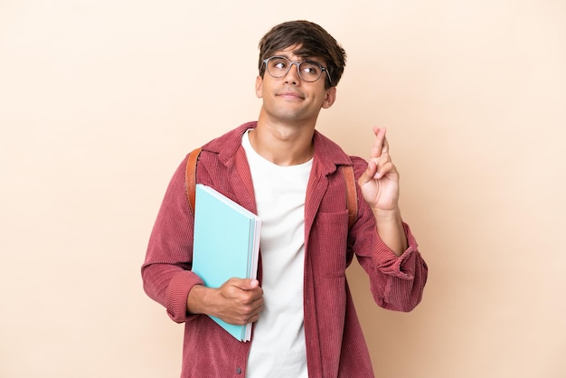 Young student caucasian man isolated on ocher background with fingers crossing and wishing the best