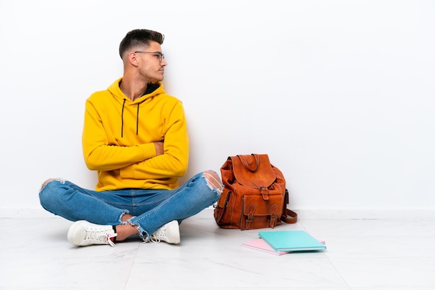 Young student caucasian man sitting one the floor isolated on white background in lateral position