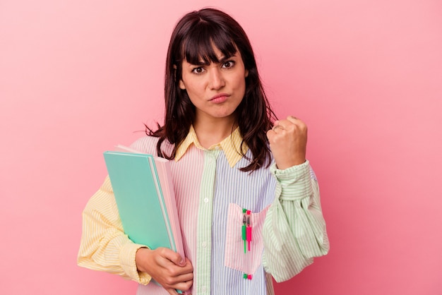 Young student caucasian woman holding books isolated on pink background showing fist to camera, aggressive facial expression.