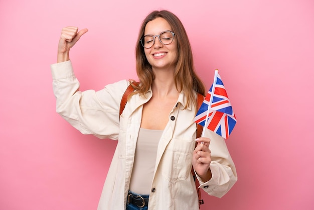 Young student caucasian woman holding an united kingdom flag isolated on pink background doing strong gesture