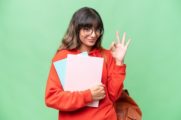 Giovane studente donna caucasica su sfondo isolato che mostra segno ok con le dita