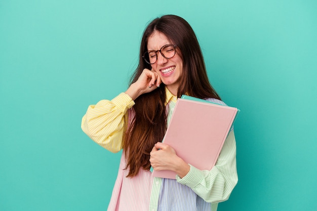 Young student caucasian woman isolated on blue background covering ears with hands.