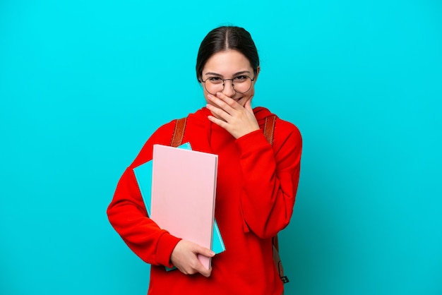 青の背景に分離された若い学生白人女性幸せと手で口を覆っている笑顔