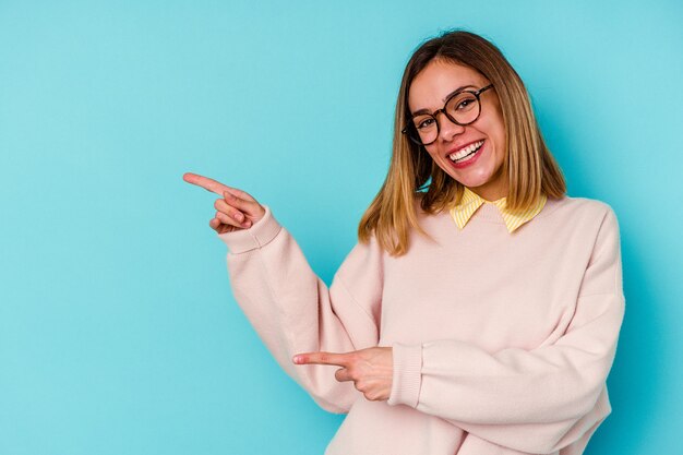 Young student caucasian woman isolated on blue excited pointing with forefingers away.