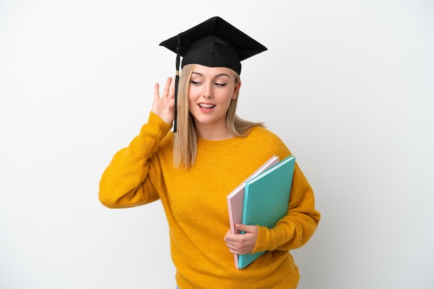 Young student caucasian woman isolated on white background listening to something by putting hand on the ear