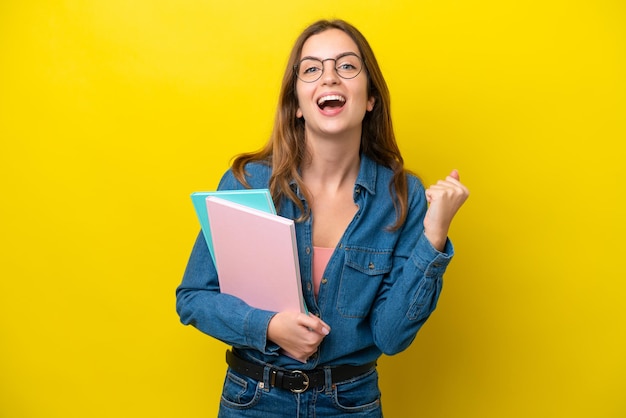 Young student caucasian woman isolated on yellow background celebrating a victory in winner position