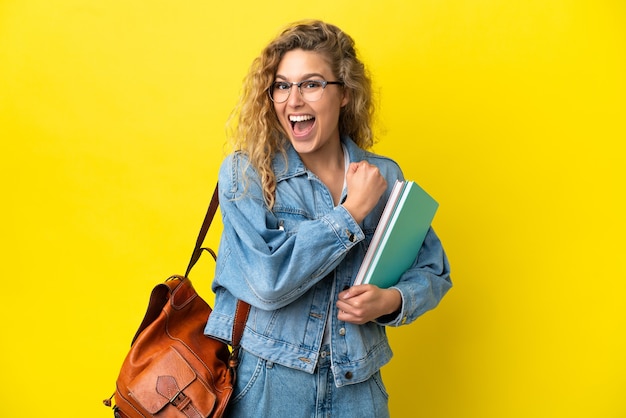 Young student caucasian woman isolated on yellow background celebrating a victory