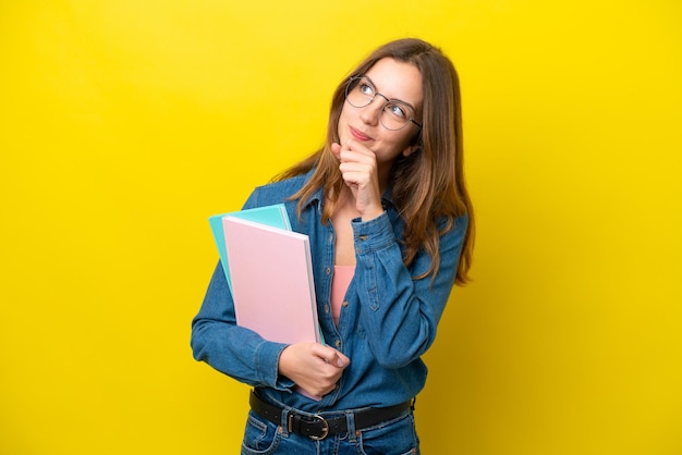 Young student caucasian woman isolated on yellow background and looking up