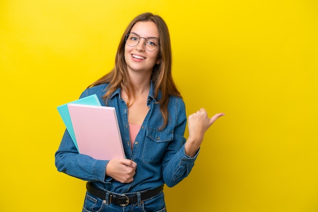 Young student caucasian woman isolated on yellow background pointing to the side to present a product