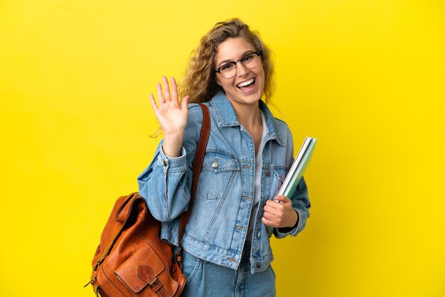 Young student caucasian woman isolated on yellow background saluting with hand with happy expression