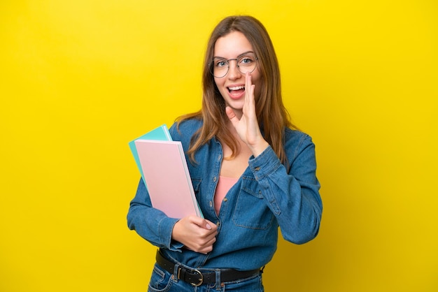 Young student caucasian woman isolated on yellow background shouting with mouth wide open
