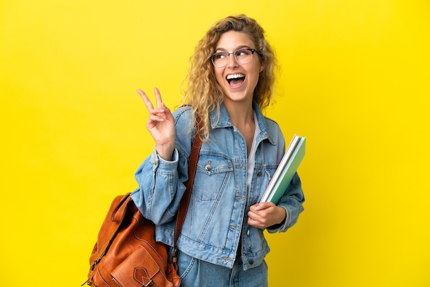 Donna caucasica del giovane studente isolata su fondo giallo che sorride e che mostra il segno di vittoria