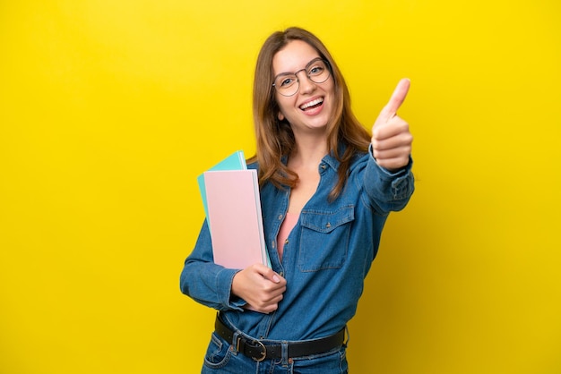 Young student caucasian woman isolated on yellow background with thumbs up because something good has happened