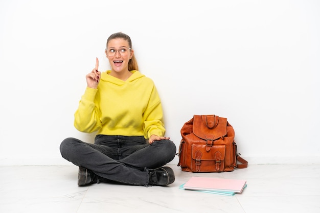 Young student caucasian woman sitting one the floor isolated on white background intending to realizes the solution while lifting a finger up