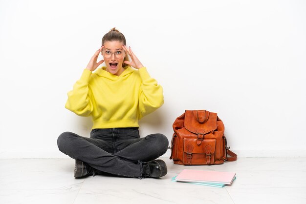 Young student caucasian woman sitting one the floor isolated on white background with surprise expression