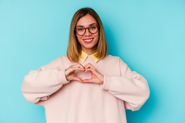 Young student caucasian woman   smiling and showing a heart shape with hands.