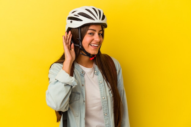 Young student caucasian woman wearing a bike helmet isolated on yellow background trying to listening a gossip.