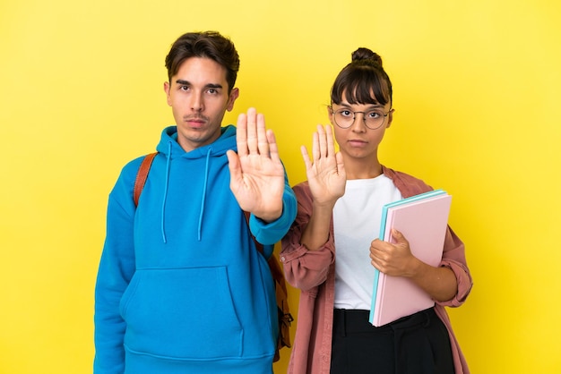 Photo young student couple isolated on yellow background making stop gesture denying a situation that thinks wrong