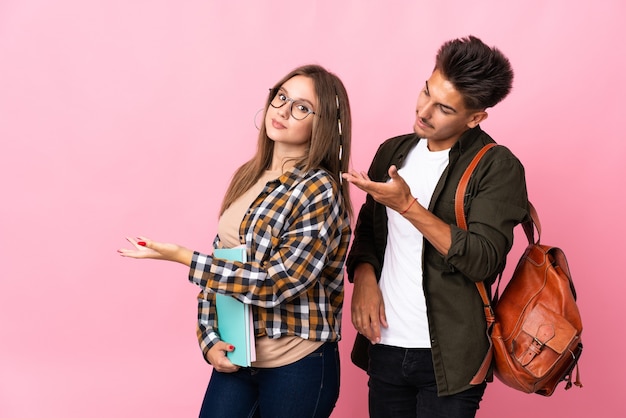 Young student couple on white pointing back and presenting a product