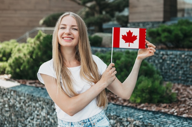 Young student girl shows a small canadian flag and stands against the background of the university