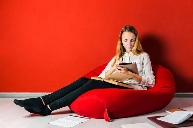 Young student girl studying sitting on the bagchair near books and tablet pc