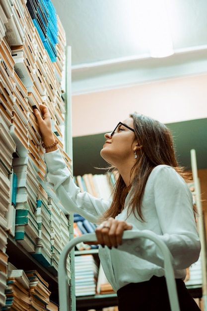 クラスのレポートを準備するために文学を探している大学図書館の若い学生の女の子