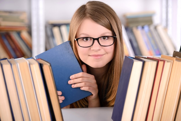 本選択本棚を持つ若い学生の女の子。