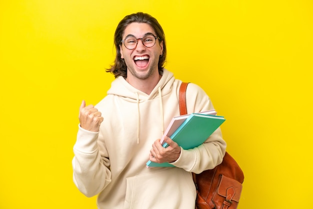 Young student handsome man isolated on yellow background celebrating a victory in winner position