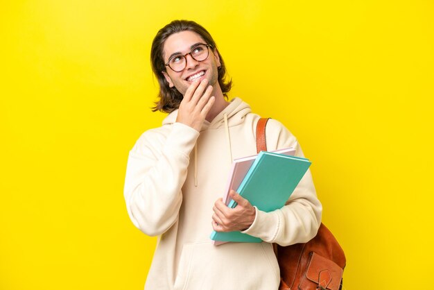 Young student handsome man isolated on yellow background looking up while smiling