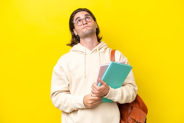 Young student handsome man isolated on yellow background and looking up