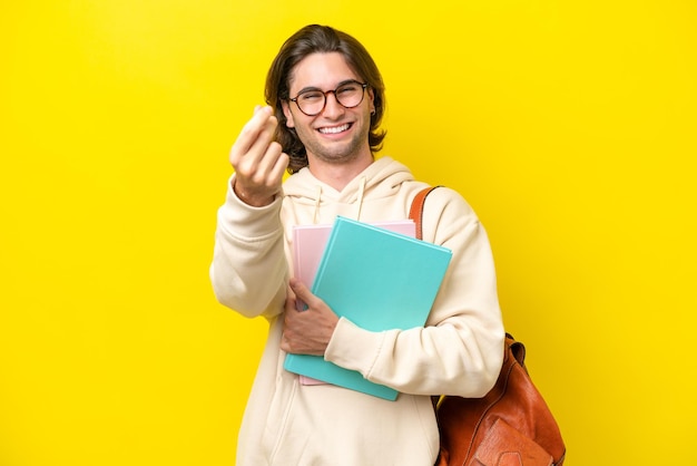 Giovane studente bell'uomo isolato su sfondo giallo che fa gesto di denaro